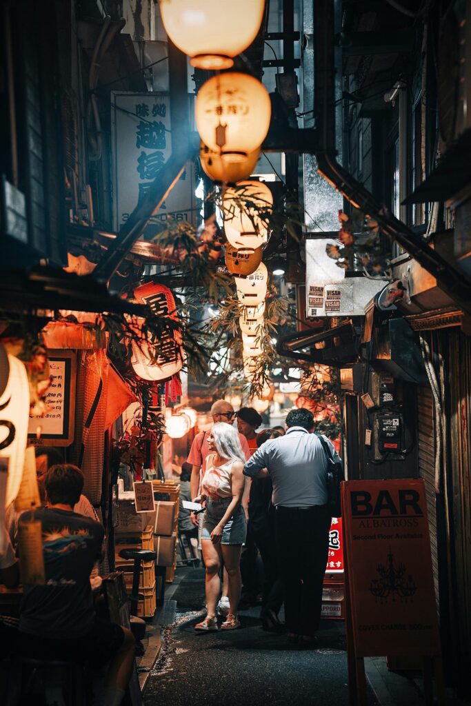 Explore the vibrant and illuminated nightlife of Tokyo's narrow streets with lanterns and crowds.