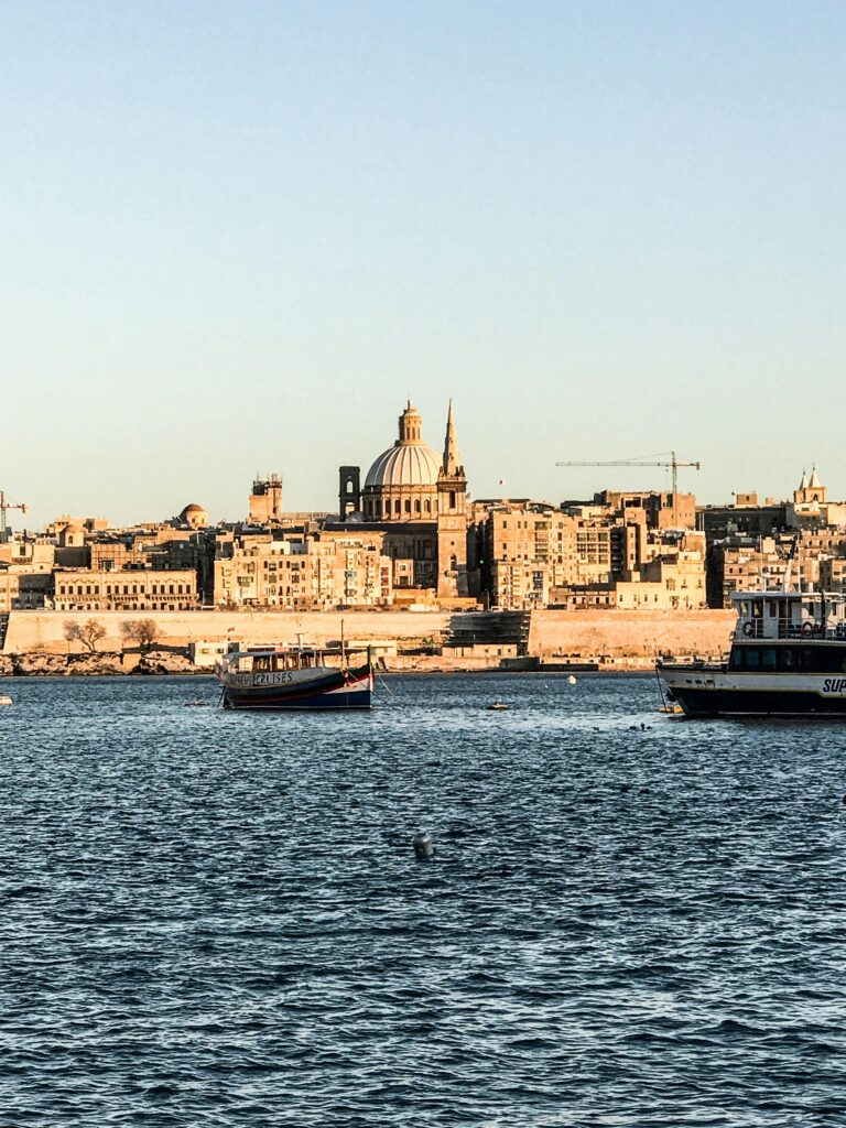 A picturesque view of Valletta's waterfront with historic architecture and boats, under clear skies.