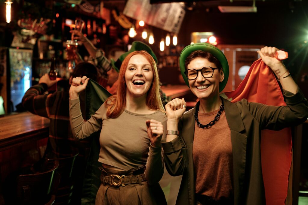 Two women celebrate St. Patrick's Day with flags at a lively bar.